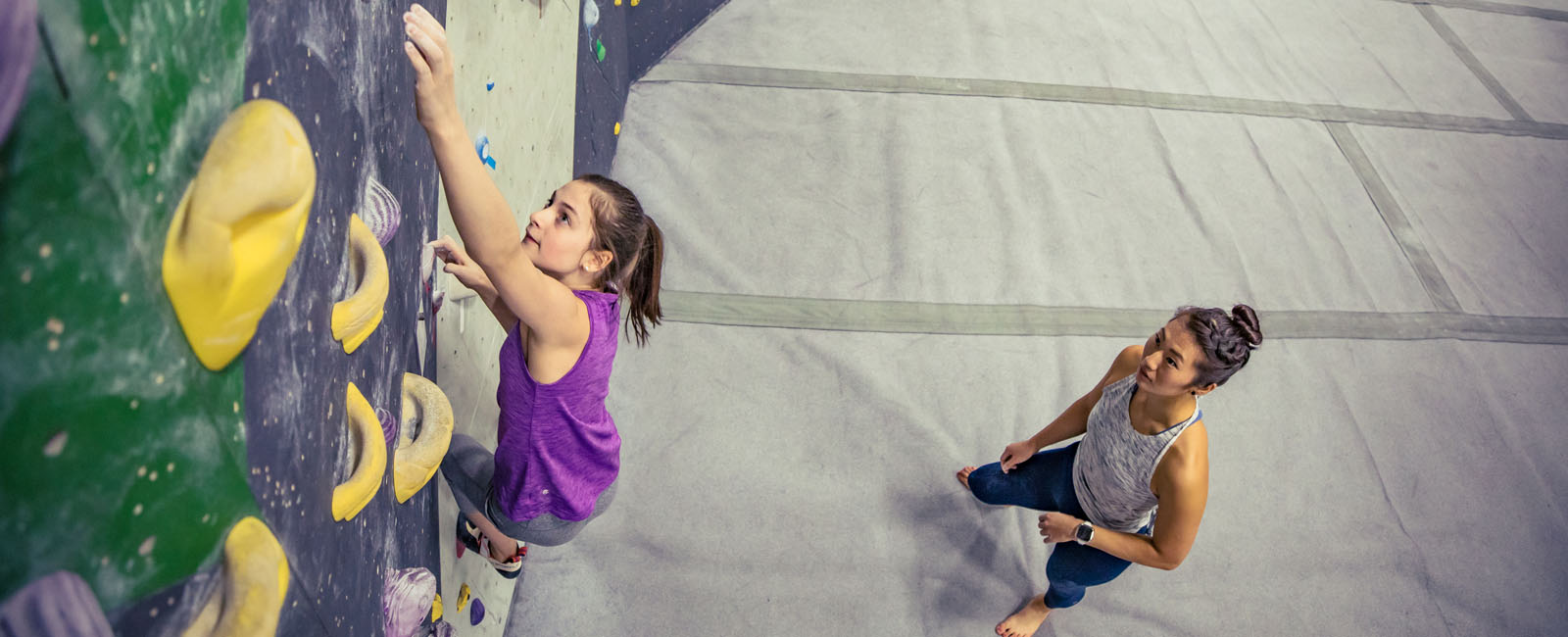 young girl bouldering with woman watching
